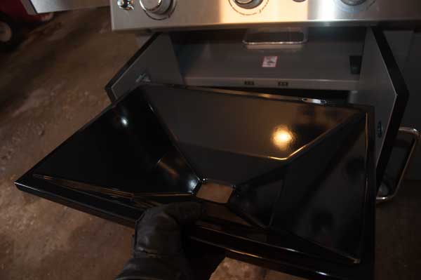 A hand with a glove holds a shiny, black, metal tray with a whole at the bottom.