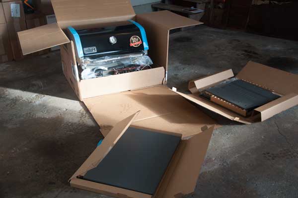 A black gas grill partially unpacked from various cardboard boxes.
