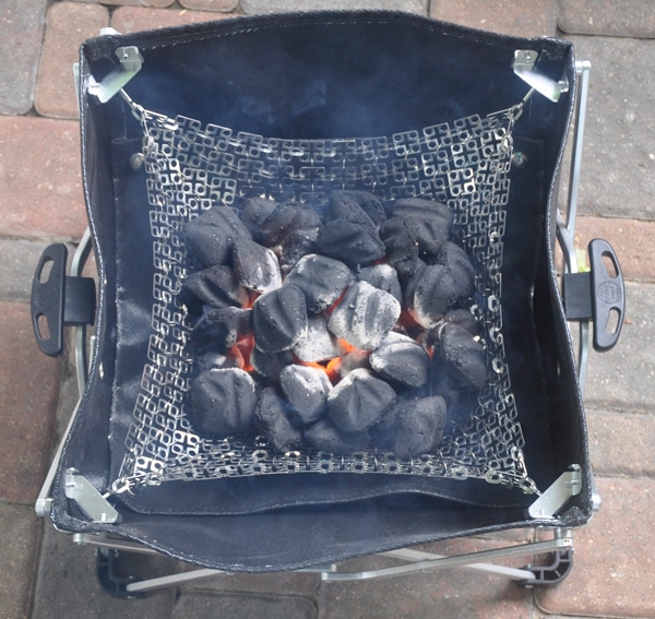 Black leathery basket with charcoal inside. A red hot fire is starting in the center of the charcoal.