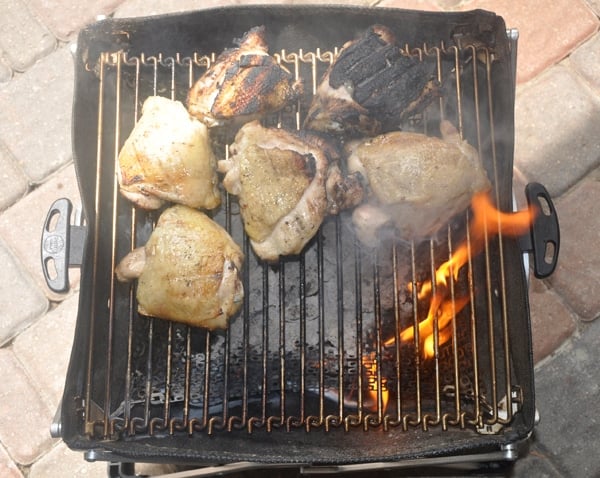 Chicken thighs on a small grill. There is a grease fire and some thighs are burnt.