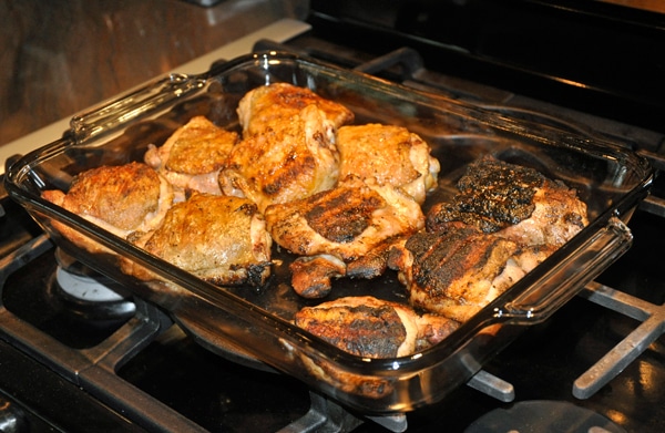 Grilled chicken in a glass tray placed on a kitchen stove top.