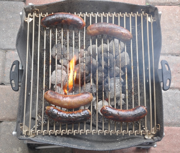 Five sausages cooking on a small BBQ grill.