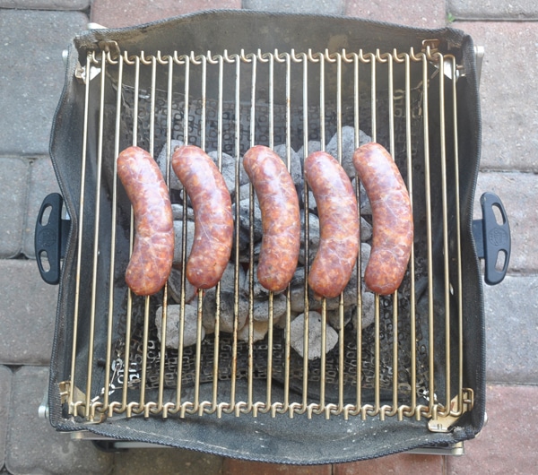 Five raw sausages placed on a small BBQ grill.