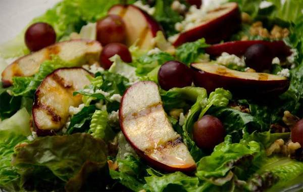 Grilled apple slices and red grapes on a bed of lettuce