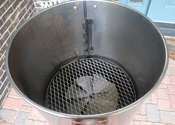 Inside of a metal barrel. A spiral metal disc and round grate are at the bottom.