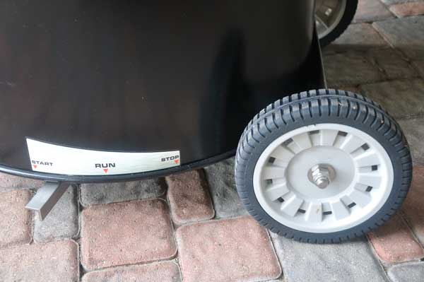 The bottom of a black metal barrel with large, plastic wheels