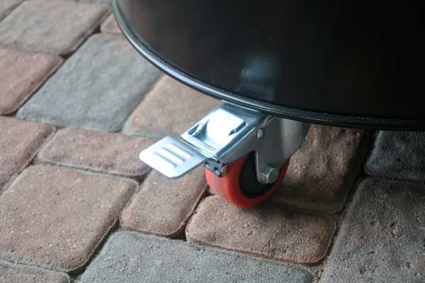 The bottom of a black metal barrel on a red, locking caster.