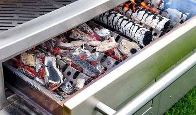 Shiny steel drawer pulled out from under a flay cooking grate filled with burning wood.