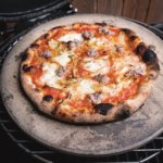 Grilled pizza on a pizza stone, sitting on round grill grate