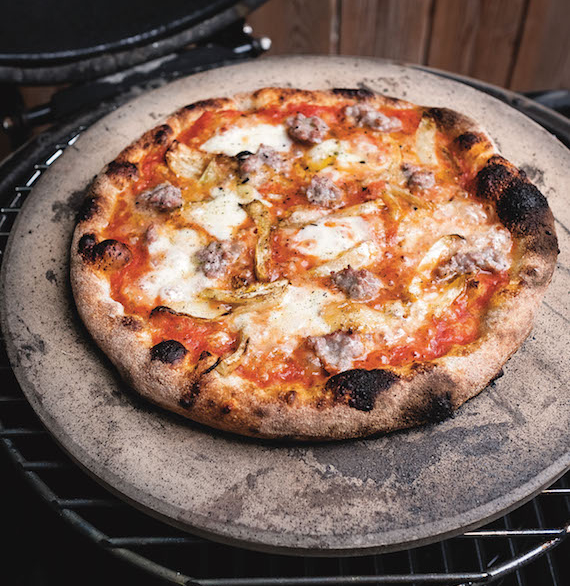 Grilled pizza on a pizza stone, sitting on round grill grate