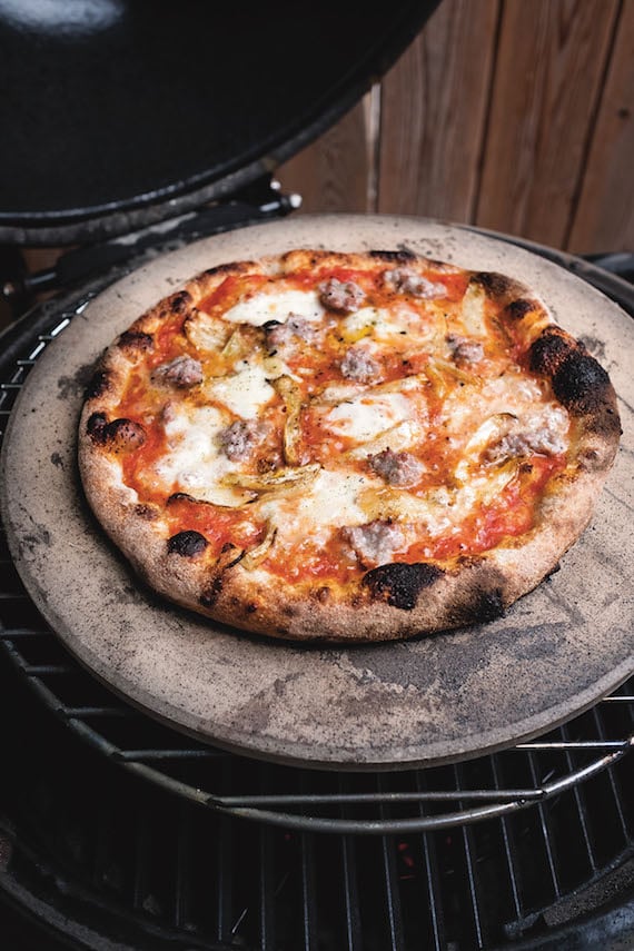 Grilled pizza on a pizza stone, sitting on round grill grate