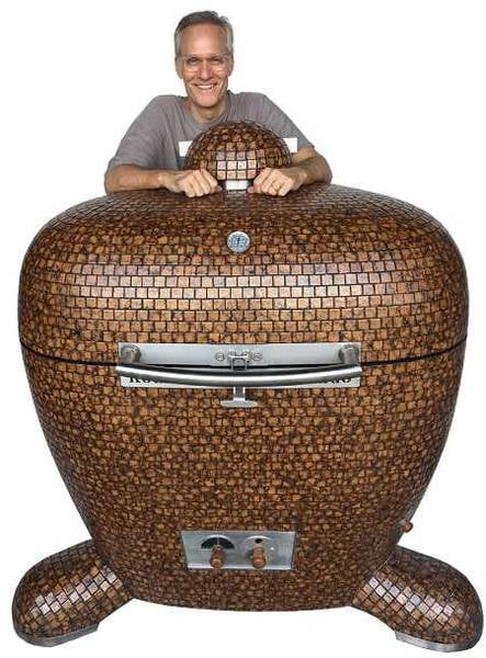Smiling man wearing a gray T-shirt stands behind an enormous kamado decorated with beautiful bronze tiles.