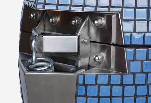 Shiny steel hinge with a large spring attached to an object covered with small blue tiles.