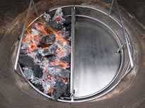A round steel basket filled with burning charcoal. A half-moon shaped piece of steel covers the right side.