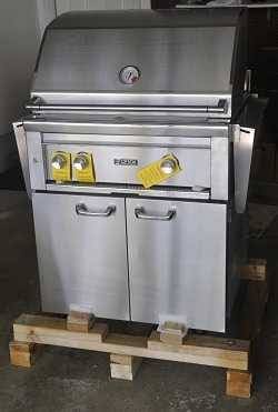 Shiny stainless steel gas grill with three gas knobs in front with yellow tags hanging from them. The grill is on a wood shipping pallet.