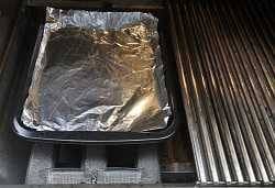 A rectangular pan covered with aluminum foil resting on a fork shaped metal object.