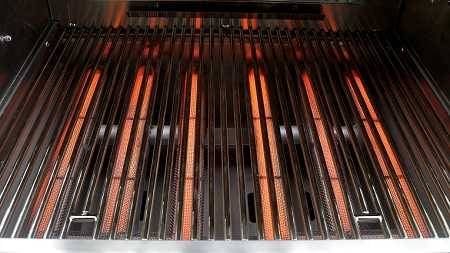 Six glowing red gas burners in a gas grill covered by steel rod grill grates.