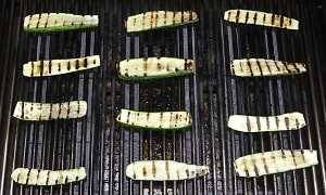 12 pieces of zucchini sliced in half, with grill marks on a gas grill.