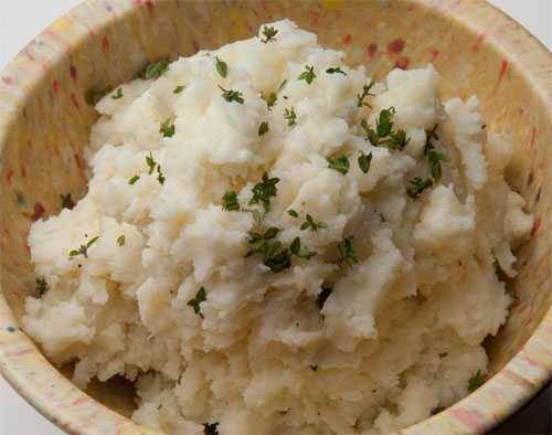 A mound of garlic mashed potatoes, garnished with herbs
