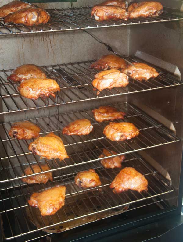 Chicken parts cooking on three racks inside a cabinet