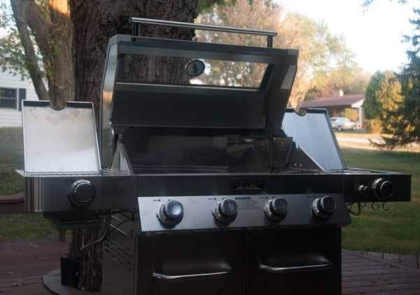 Shiny steel gas grill on an outdoor deck. The lid is up showing a window cut into it.