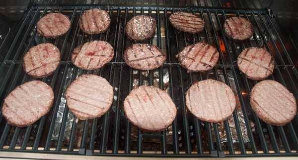 Hamburger patties cooking on a grill grate. The burgers in the back are almost done while the ones up front are still raw.