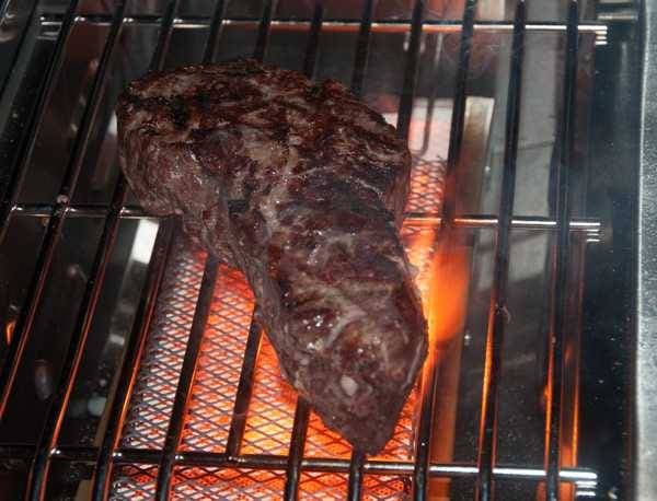 A steak sizzling over a red hot rectangular burner.