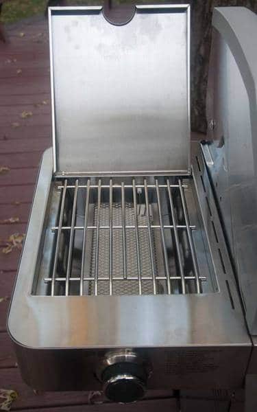 A shiny metal box with a hinged lid. The lid is up showing a white rectangular object inside covered by a steel rod grate.