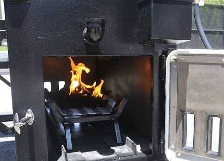 A black cabinet with open door. A wood fireplace rack is inside. A small pile of charcoal is burning on the rack.