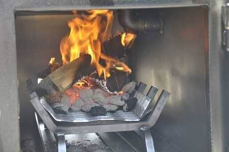 A black cabinet with open door. A wood fireplace rack is inside. A small pile of charcoal and a couple logs are burning on the rack.