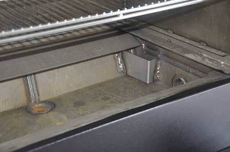 An empty water trough, black on the outside and slightly rusted steel on the inside.