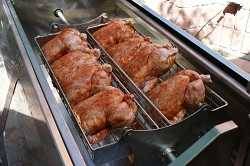 Large rectangular metal trough with large motorized rotisserie cooking chickens.