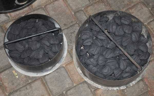 small barrel smoker's charcoal basket filled with charcoal next to larger smoker's full charcoal basket.