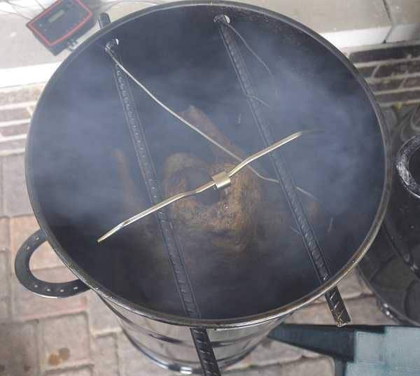 Barrel smoker from above, lid off. A large turkey hangs from two bars as smoke swirls around.
