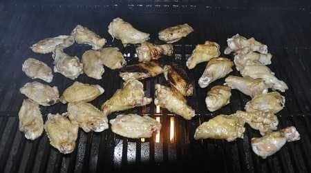 Chicken wings cooking on a grill at night. A bright fire is concentrated in the middle and the wings over the fire are getting burned.