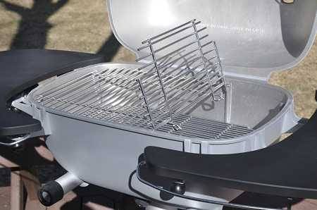 Shiny rectangular grill with lid up showing steel rod cooking grates. There are black shelves on each side. The grill is on an outdoor deck.