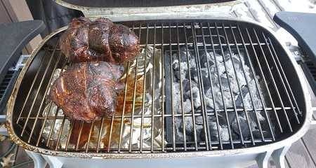 A rectangular grill with hot charcoal on the right side and two smoked hunks of meat on the cooking grate left side.