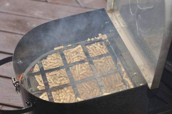 A black metal bin filled with wood pellets with smoke billowing out.