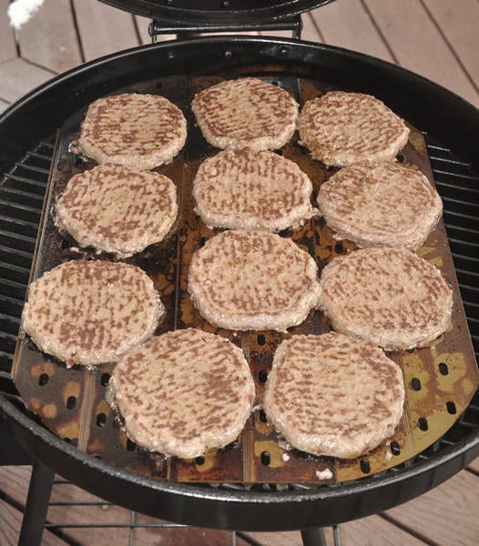 Hamburger patties cooking on a round kettle grill.