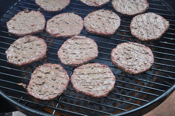Bland pale grey hamburger patties cooking on a round kettle grill.
