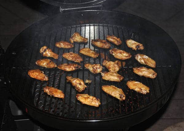 Chicken wings cooking on a round kettle grill.
