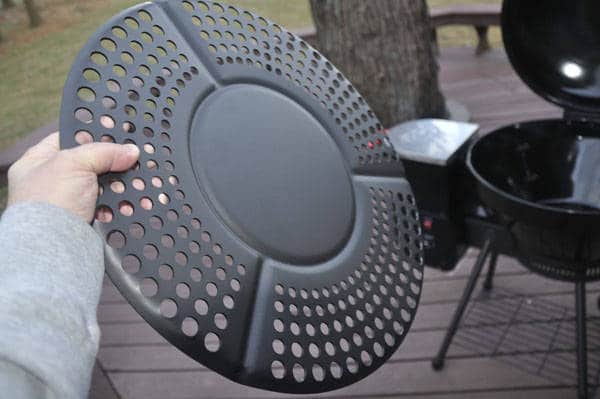 A hand holding up a round, black metal disc with holes punched out in a radial pattern.
