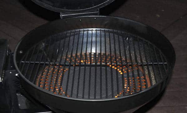 A kettle grill at night with the lid up. A glowing fire is seen within.