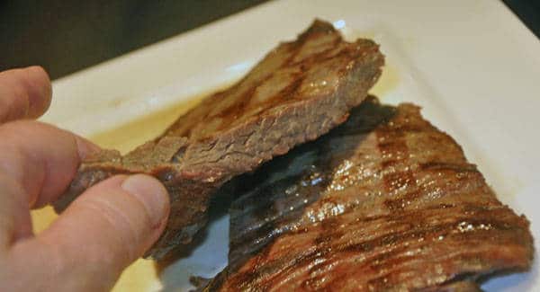 Fingers holding a piece of overdone steak