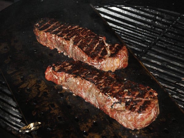 Seared steaks cooking on a round kettle grill.