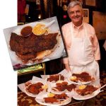 An aproned chef stands next to plates of Memphis style dry ribs