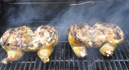 Two whole chickens cooking on a grill with lots of smoke. They are slightly charred.