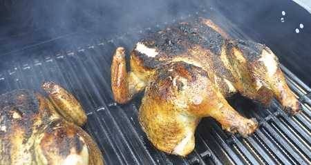 Two whole chickens cooking on a grill with lots of smoke. The skins is burned.