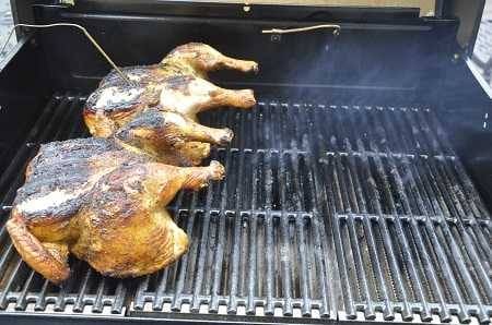 Two whole chickens on the left side of a grill. One has a thin metal rod inserted in the top. The skin is burned.
