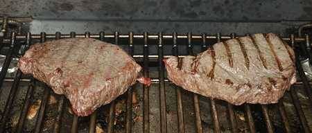 Two bland grayish steaks on a cooking grate.